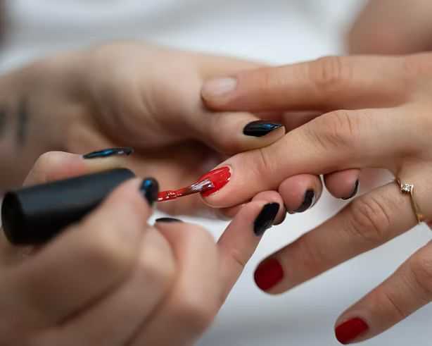 Close-up of hands applying red nail polish during a manicure session.